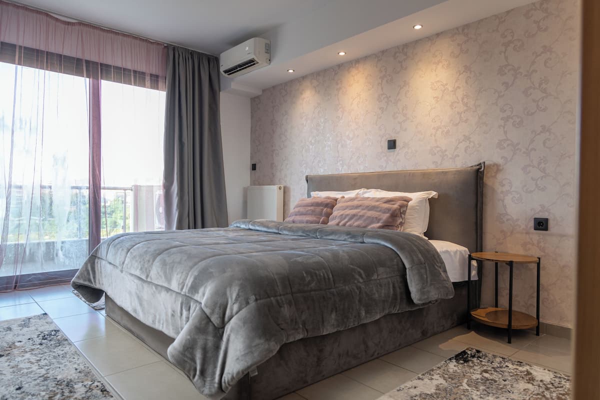 A modern bedroom with a large bed, a bedside table, and a view of the outdoors.