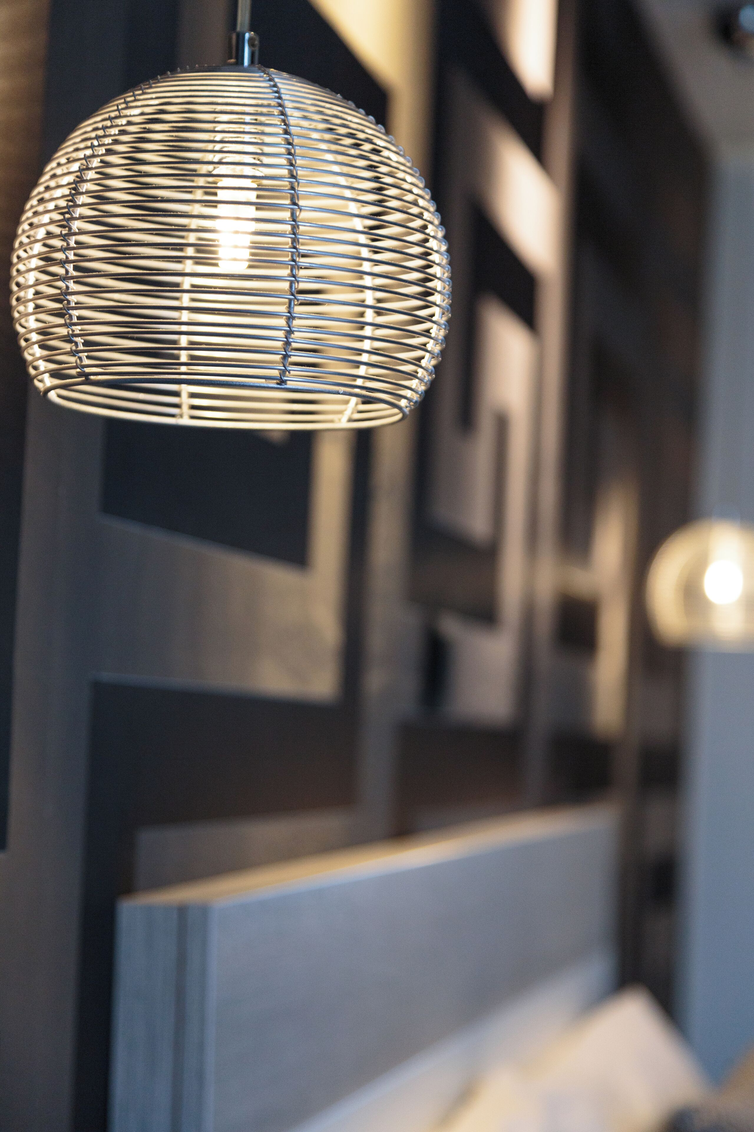 A hanging spherical light fixture with a wire design, a geometric wall pattern, and a partially visible bed with a headboard.