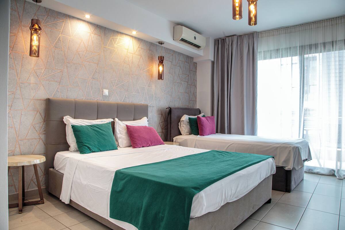 A modern hotel room with two beds, a round table, and a geometric-patterned wall.