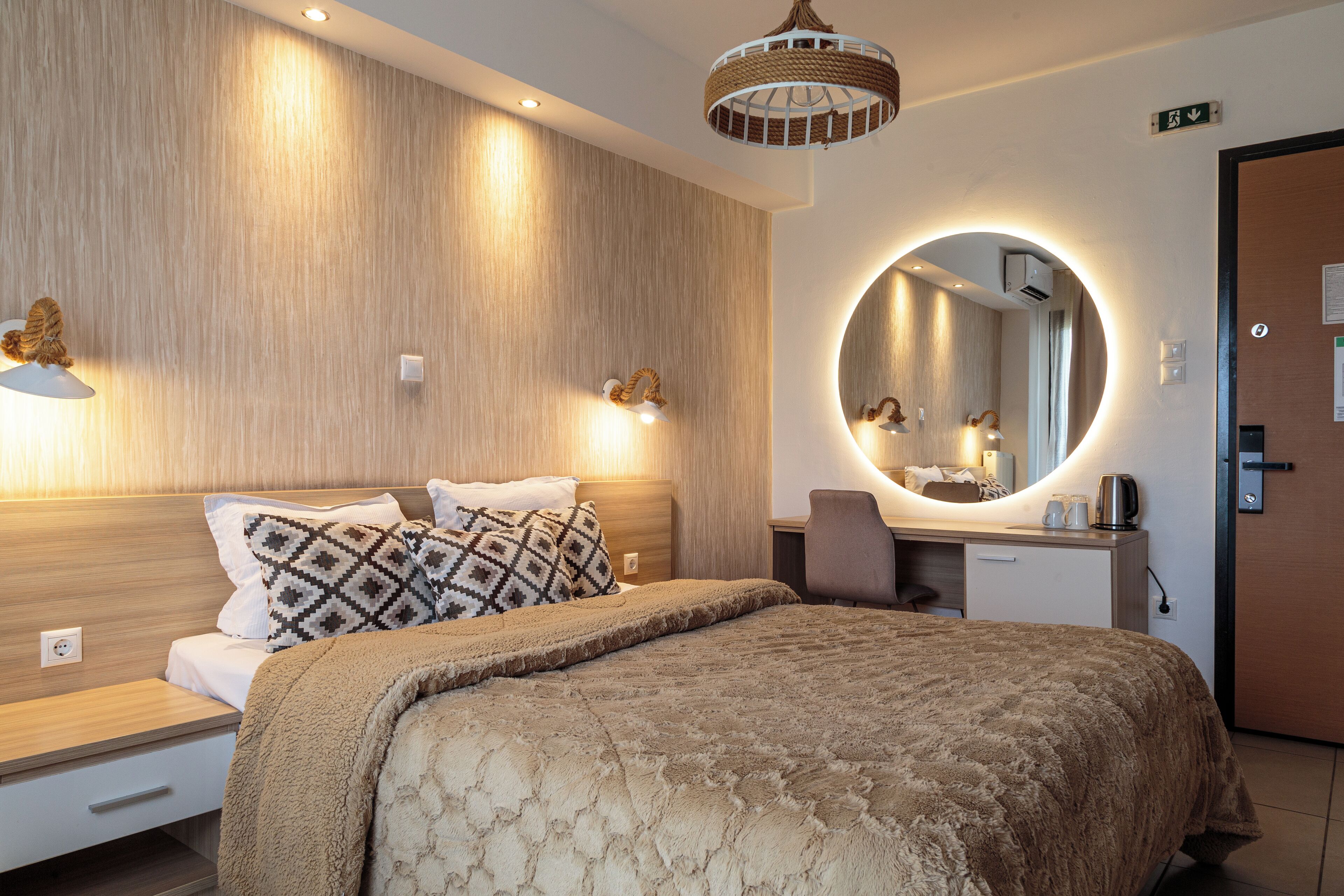 A modern hotel room with a large bed, a round mirror, a desk, and a chair.