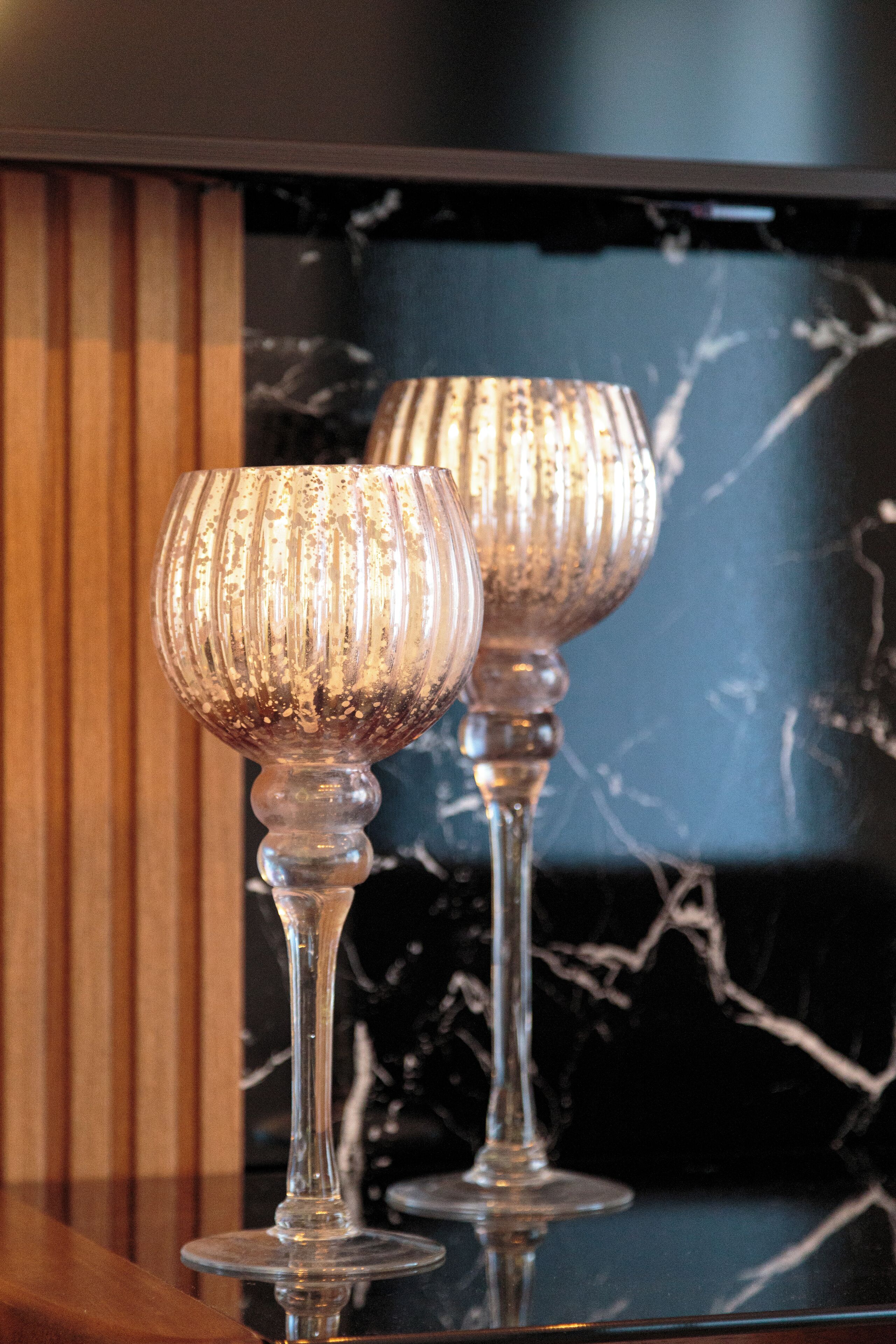 Two glass wine glasses on a reflective surface with a dark background and a wooden panel.
