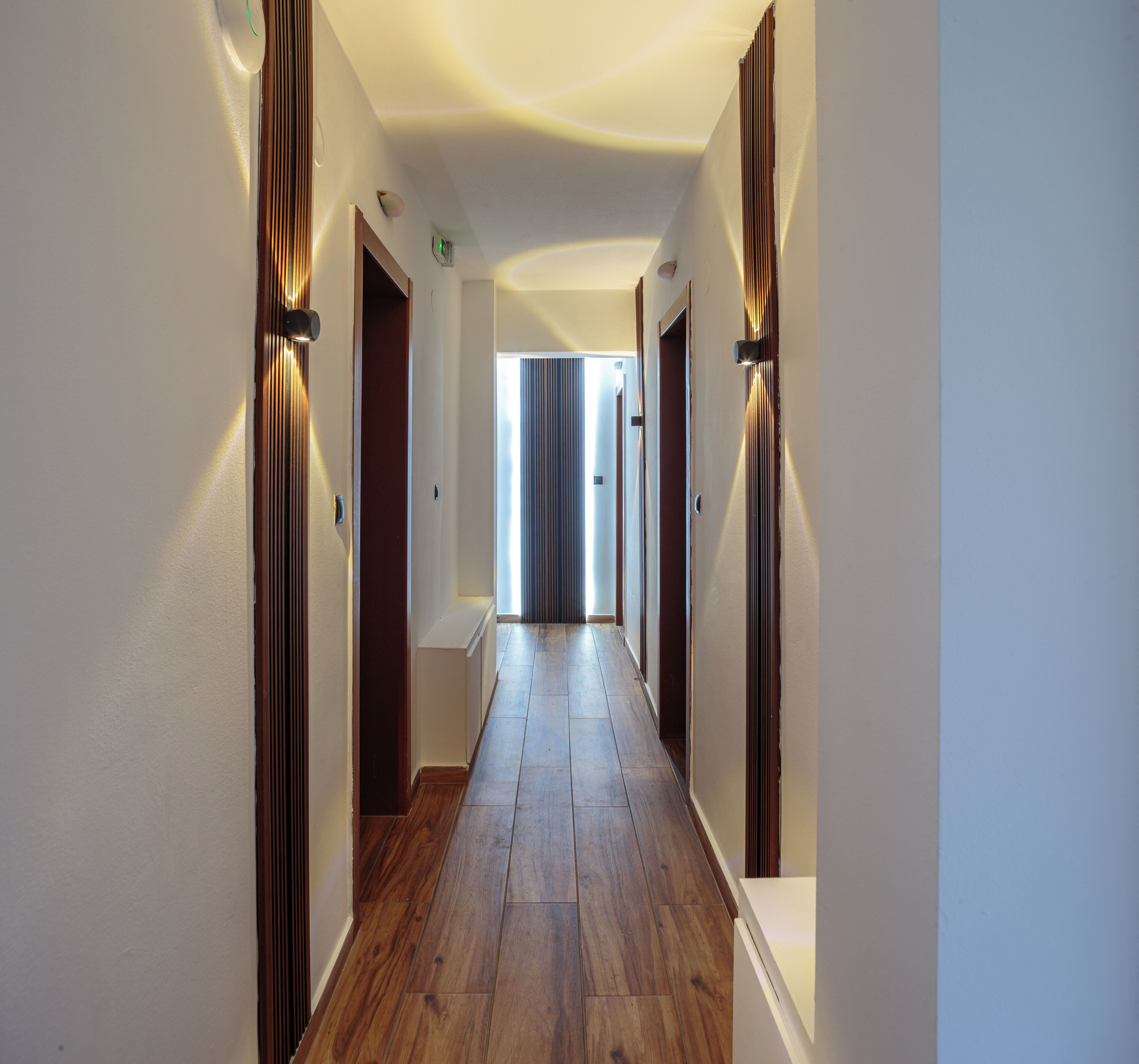 Un pasillo con suelo de madera, paredes blancas y puertas a ambos lados.