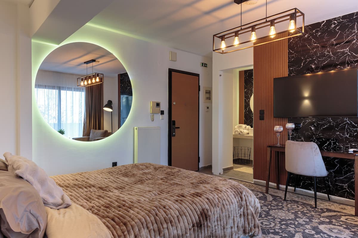 A modern hotel room with a large bed, a round mirror, a television, and a small table with a chair.