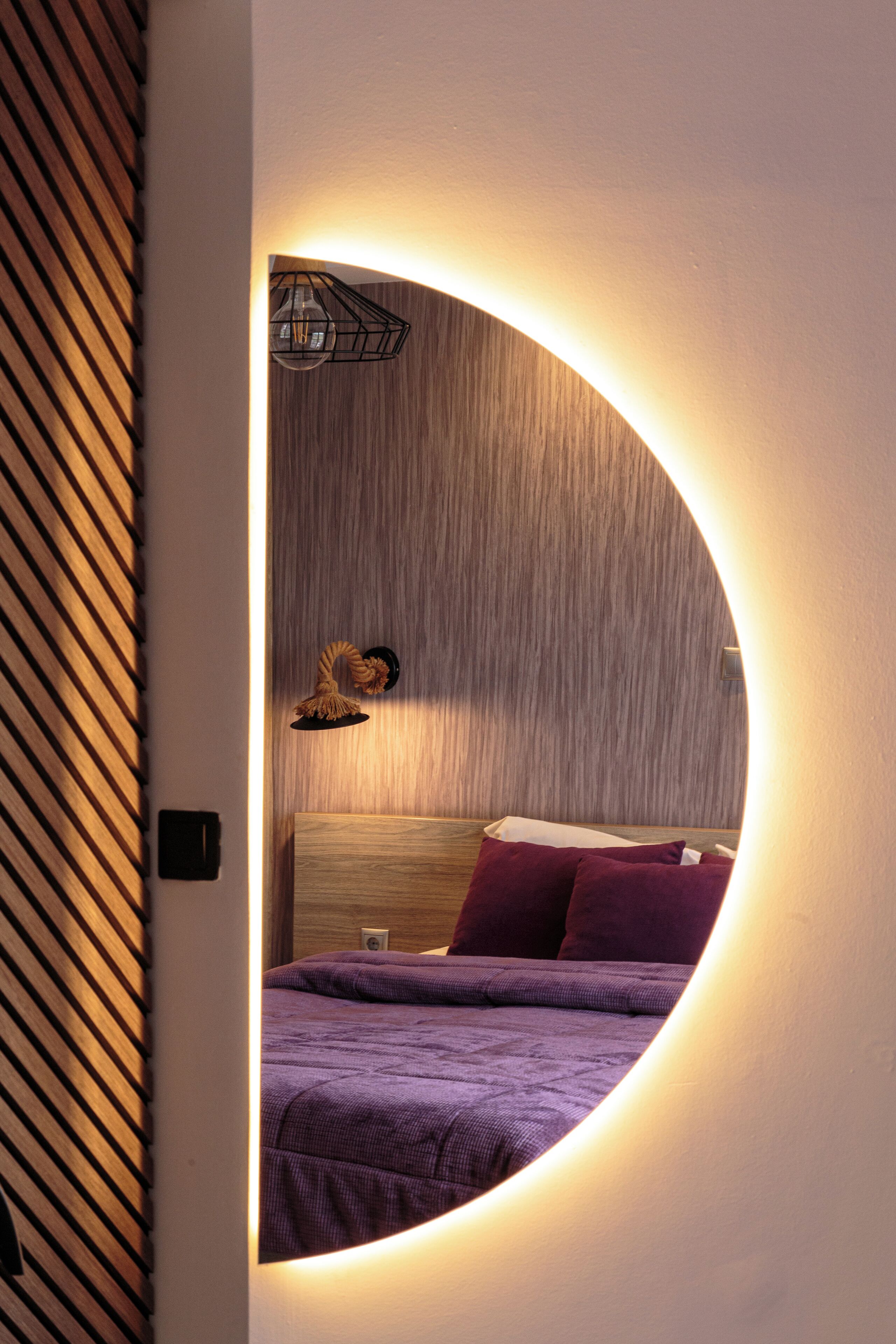 A bedroom with a circular mirror, wooden slat wall, and a bed with purple bedding.