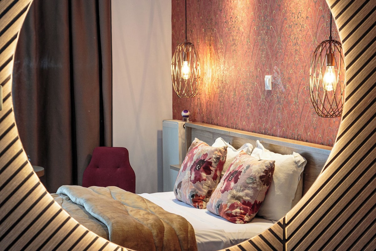 A circular mirror reflecting a modern bedroom with a bed, pillows, and a red chair.