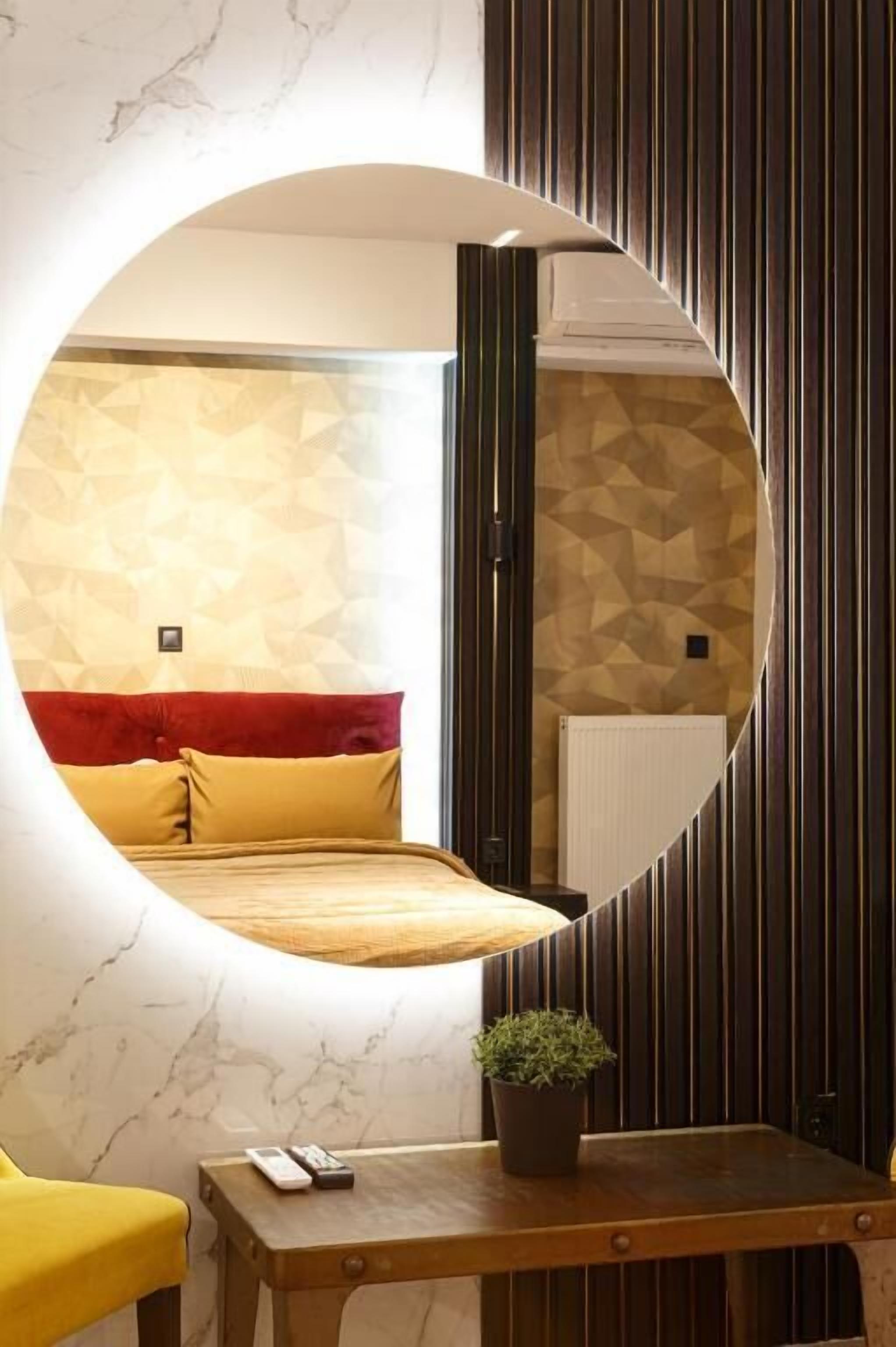 Une chambre à coucher avec un lit, une table de chevet ornée d’une plante et un miroir qui reflète la pièce.
