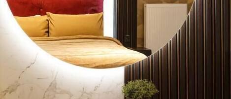 Une chambre à coucher avec un lit, une table de chevet ornée d’une plante et un miroir qui reflète la pièce.