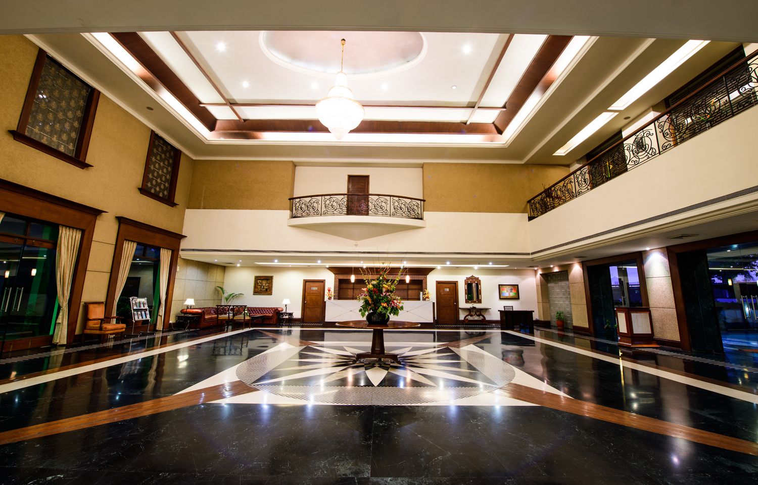 A spacious lobby with a central floral arrangement, a high ceiling with skylights, and a polished marble floor.
