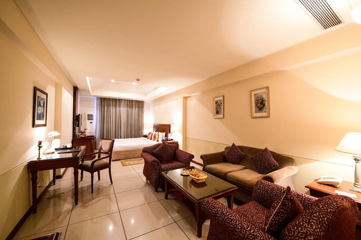 Quarto de hotel com cama, escrivaninha com cadeira, sofá e mesa de centro.