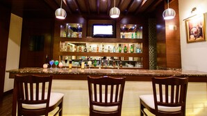 Zona de bar con vigas de madera en el techo, tres taburetes y un televisor colgado sobre la barra.