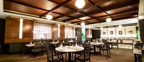 Un restaurante con vigas de madera en el techo, mesas redondas y sillas.