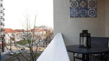 Un balcón con vistas a edificios, una pared de azulejos con adornos y una mesa con una linterna.