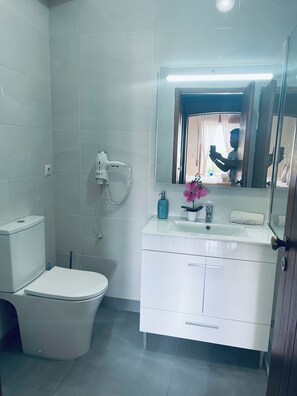 Een moderne badkamer met toilet, wastafel met spiegel en een haardroger aan de muur.