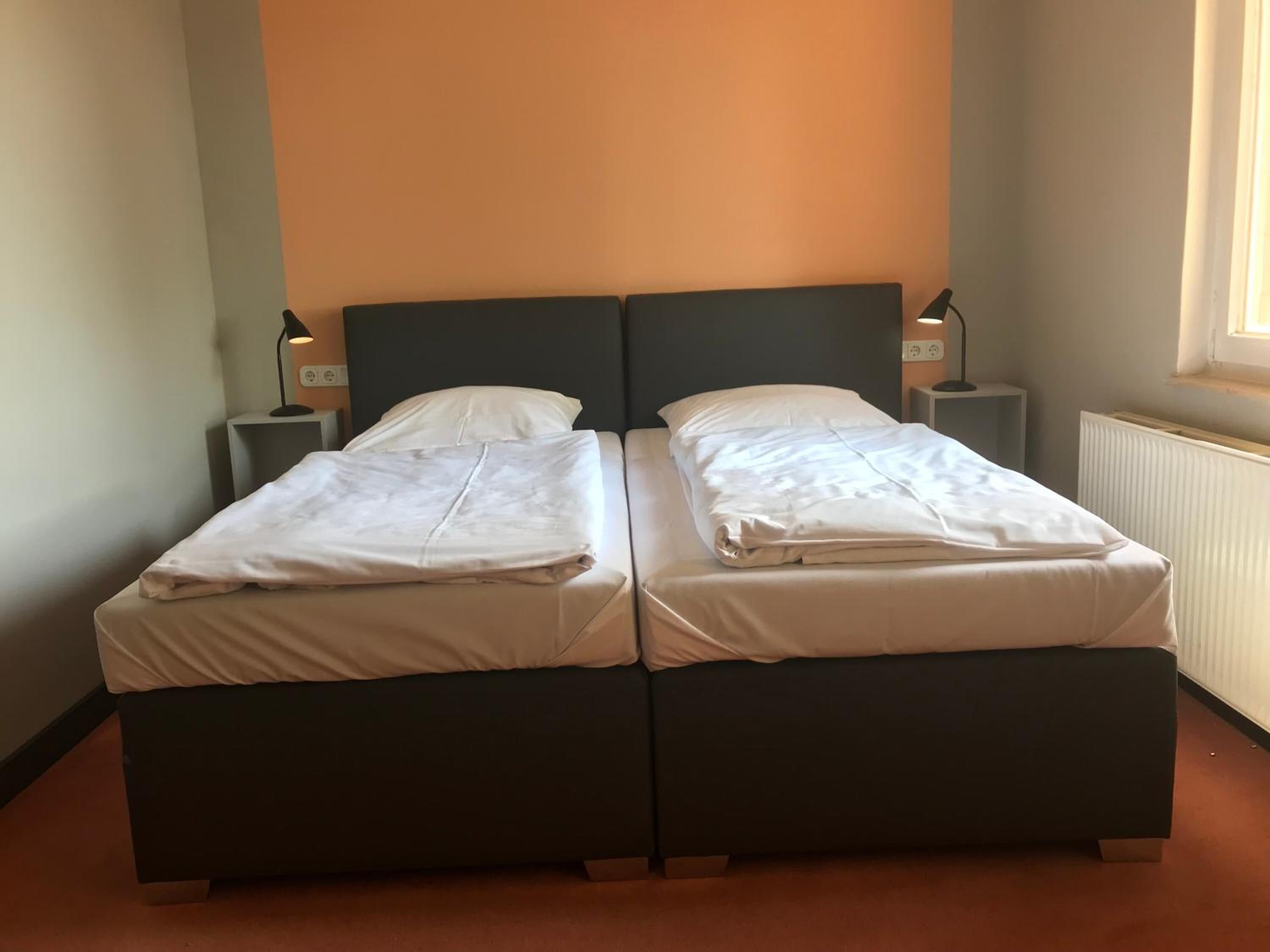 Een tweeepersoonskamer met twee bedden, elk voorzien van nachtkastje en lamp.