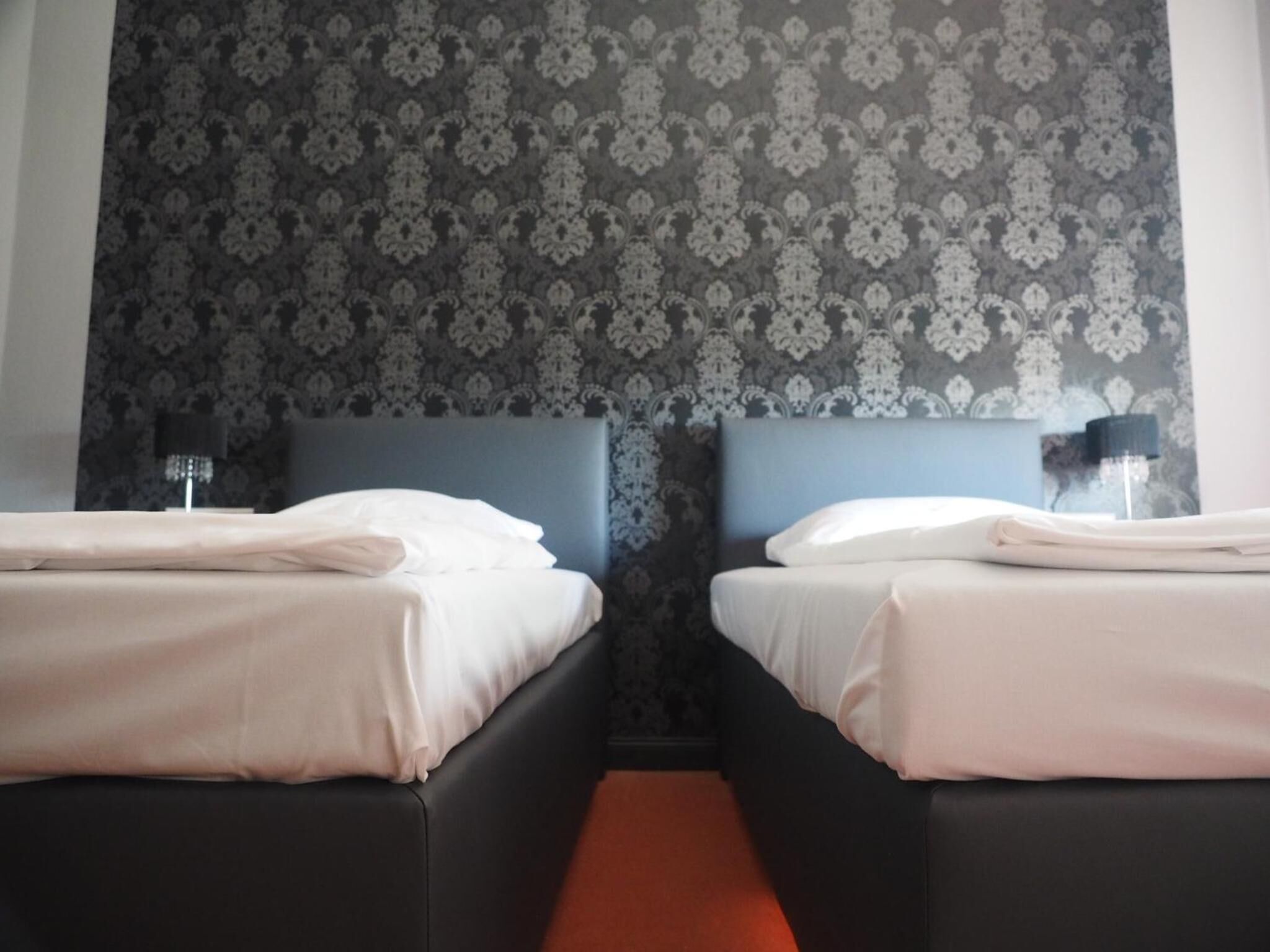 Habitación de hotel con dos camas, cabeceros oscuros y un papel tapiz estampado.