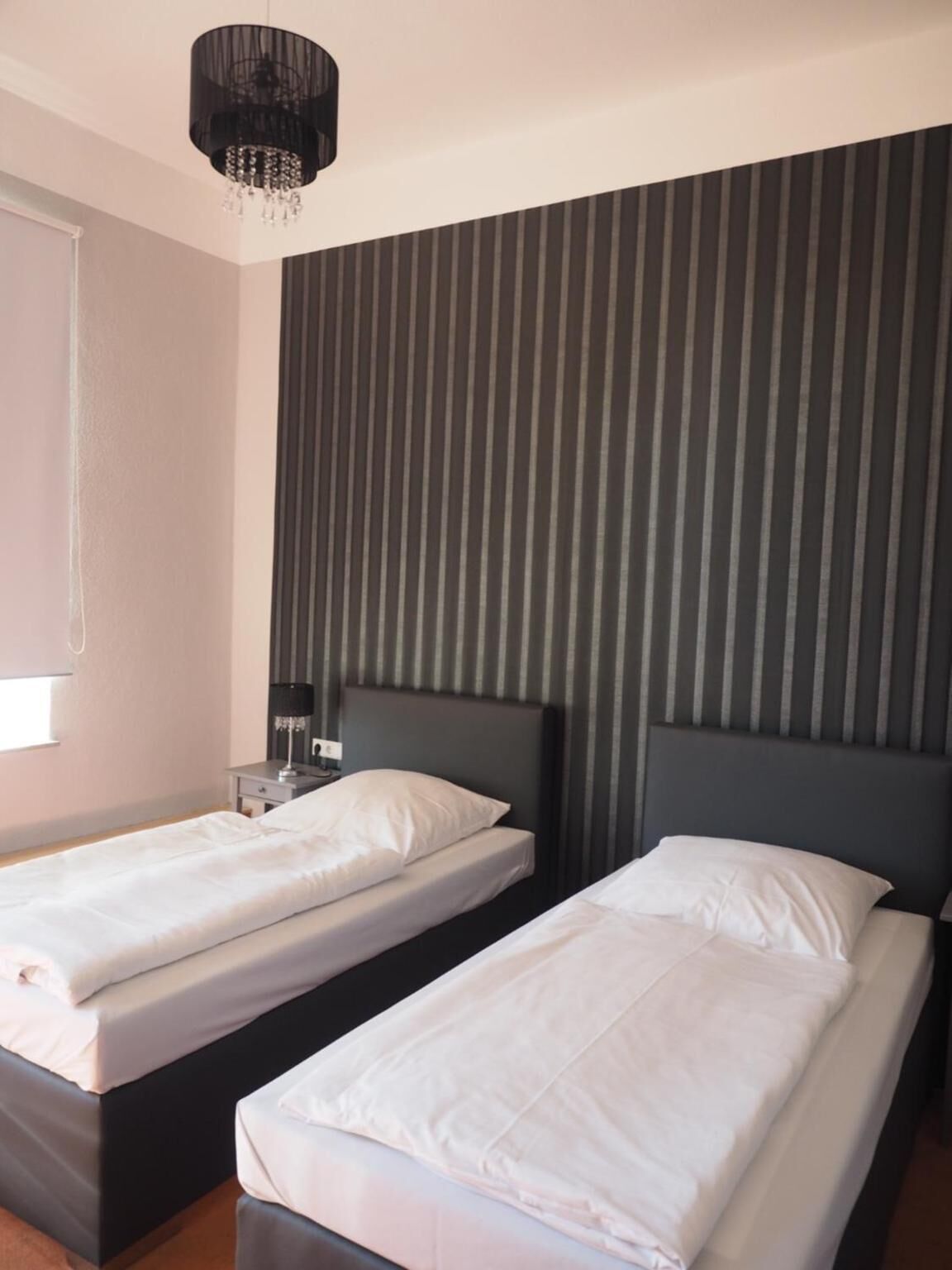 Ein Hotelzimmer mit zwei Einzelbetten, einem Nachttisch mit Lampe, einer gestreiften Wand und einer Kristallleuchtre.