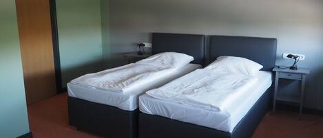 Una habitación con dos camas individuales, una mesita de noche con lámpara y una puerta.