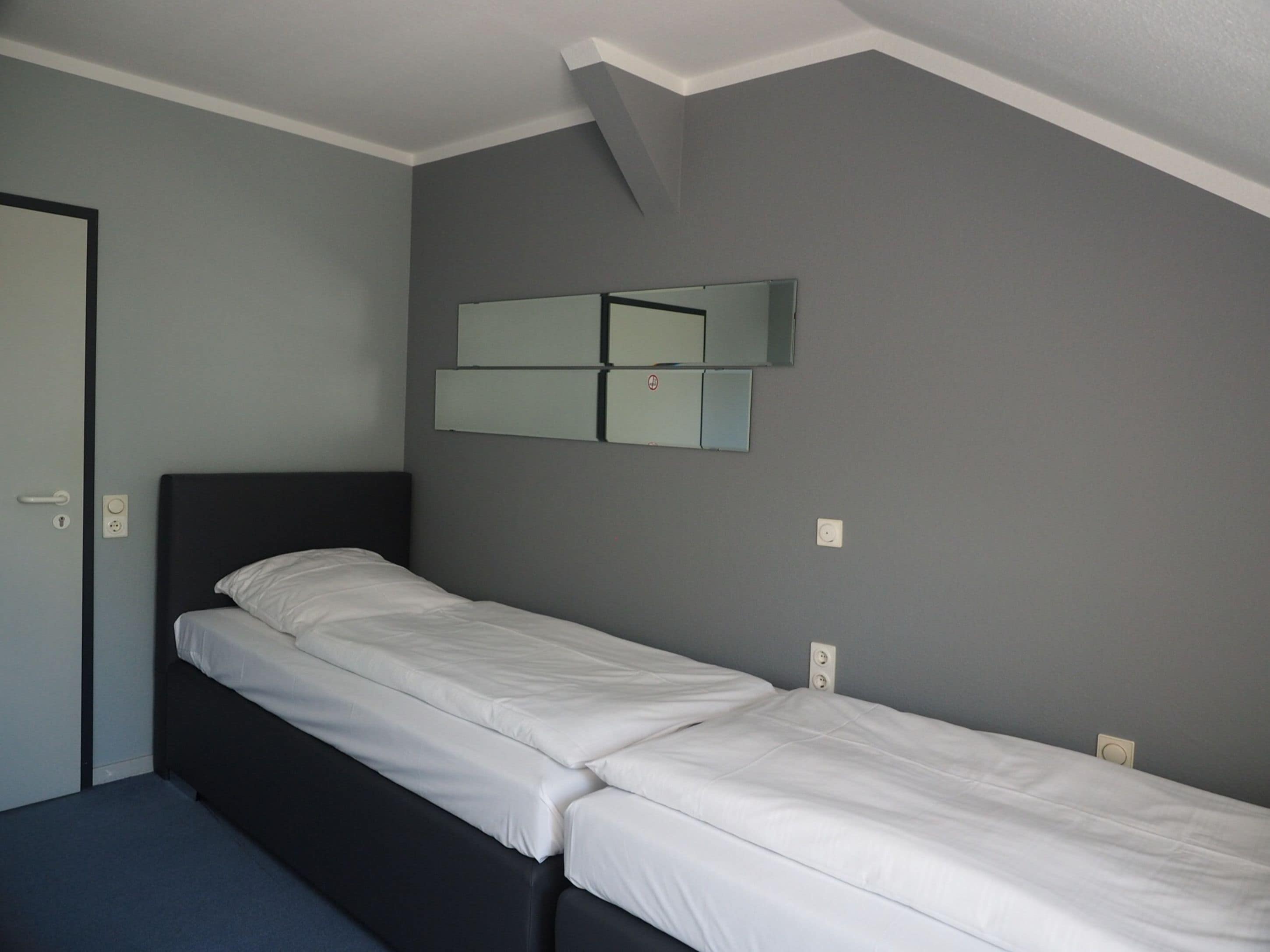 Una cama individual con ropa blanca en una habitación con paredes grises y un cabecero negro.