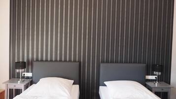Ein Hotelzimmer mit zwei Einzelbetten, einem dunkel gestreiften Kopfteil, Nachttischen mit Lampen und einem neutralen Farbkonzept.