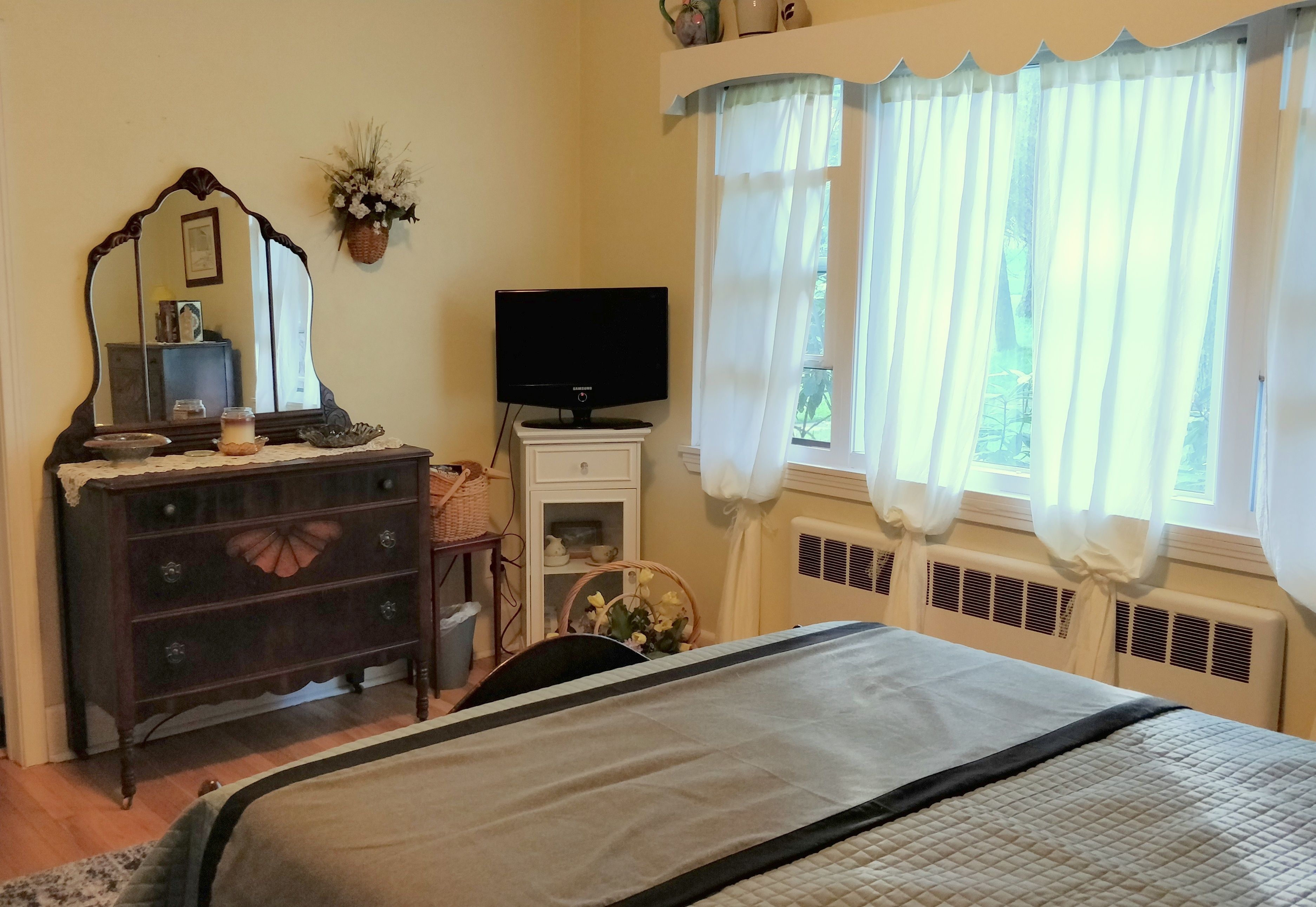A bedroom with a bed, dresser, TV, and a window with curtains.