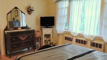 A bedroom with a bed, dresser, TV, and a window with curtains.