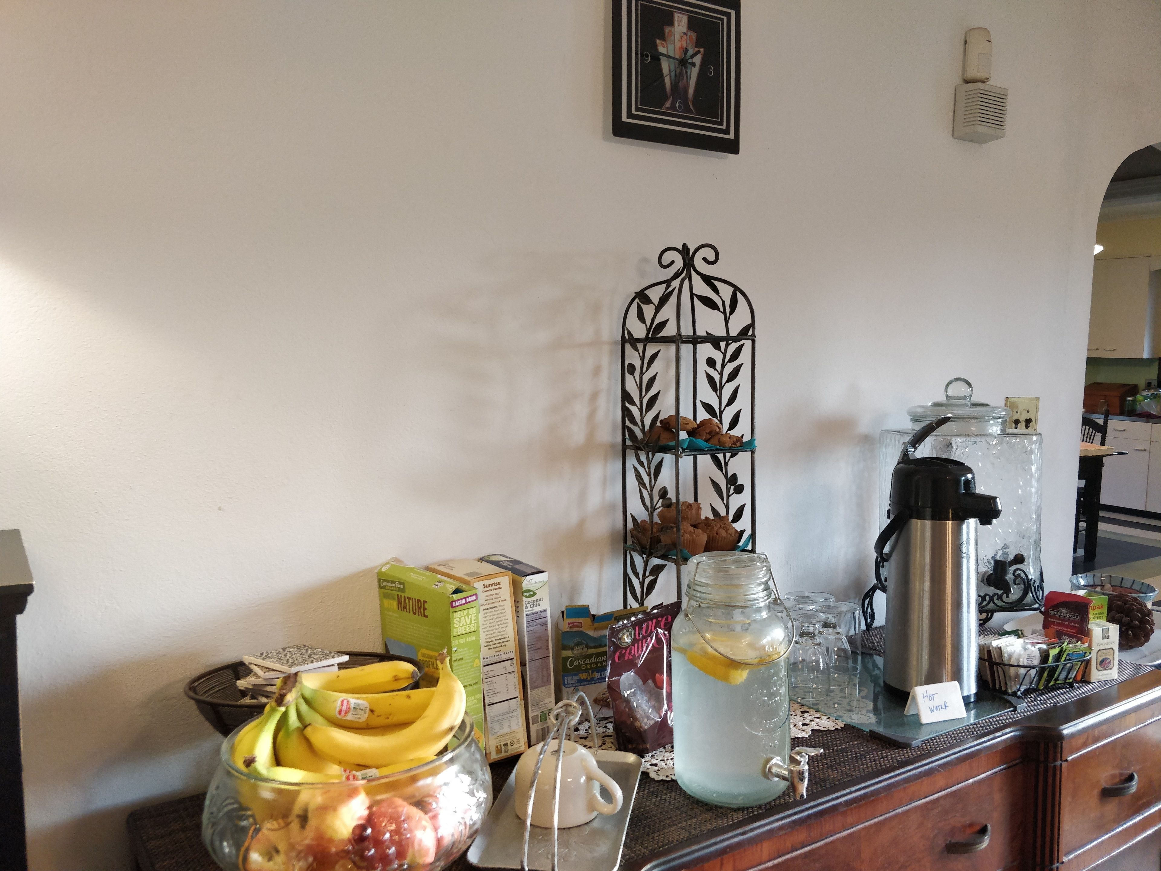 Una encimera de cocina con un frutero, una cafetera, un tarro de limonada y varios utensilios de cocina.
