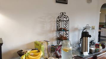 Una encimera de cocina con un frutero, una cafetera, un tarro de limonada y varios utensilios de cocina.