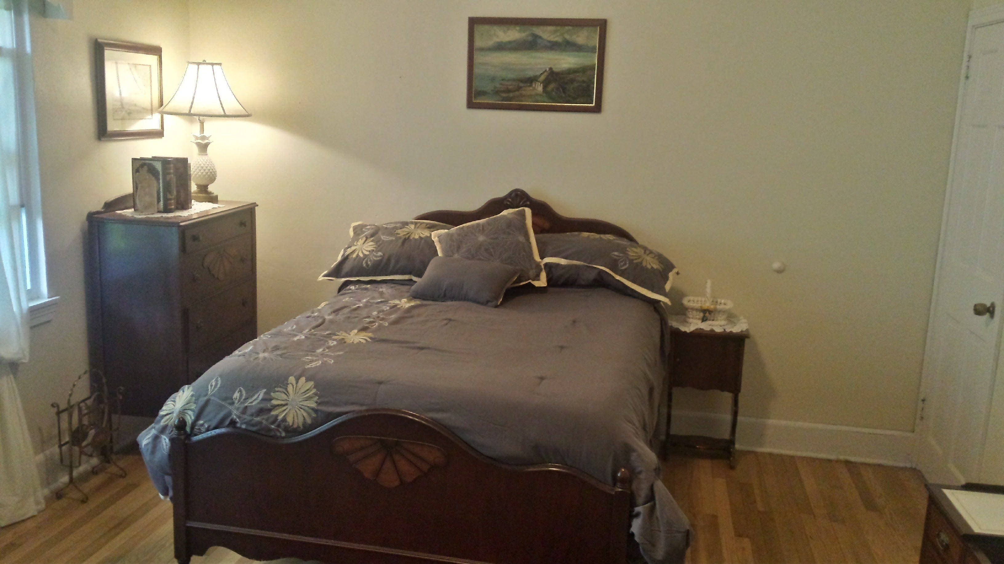 Une chambre à coucher avec un lit en bois, une table de chevet avec une lampe, une commode et un tableau encadré accroché au mur.