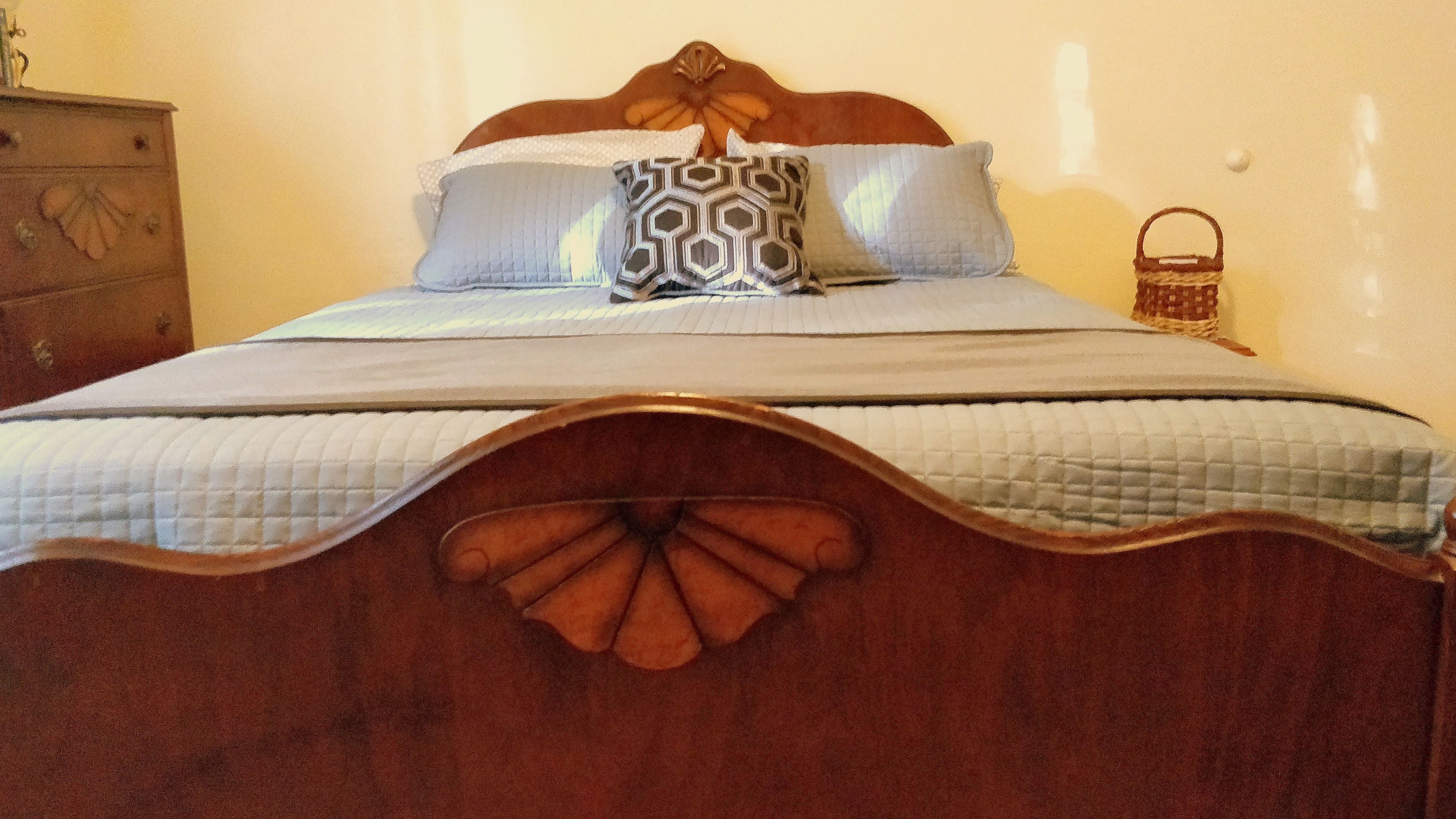 A bed with a wooden headboard featuring a leaf design, a patterned pillow, and a quilted bedspread.