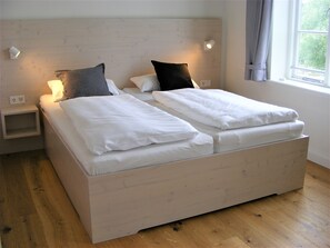 Een tweepersoonsbed met witte lakens, een nachtkastje en een wandlamp.