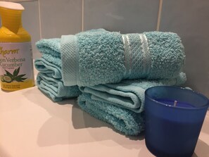 A stack of light blue towels, a blue candle, and a bottle of room fragrance. - Nice and private rooms (London)