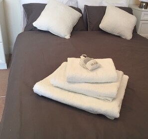 A neatly made bed with a brown bedspread, two white pillows, and a folded white towel with a tag on it. - Nice and private rooms (London)