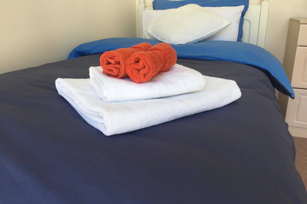 A neatly made bed with blue and white bedding, a white pillow, and two rolled towels.