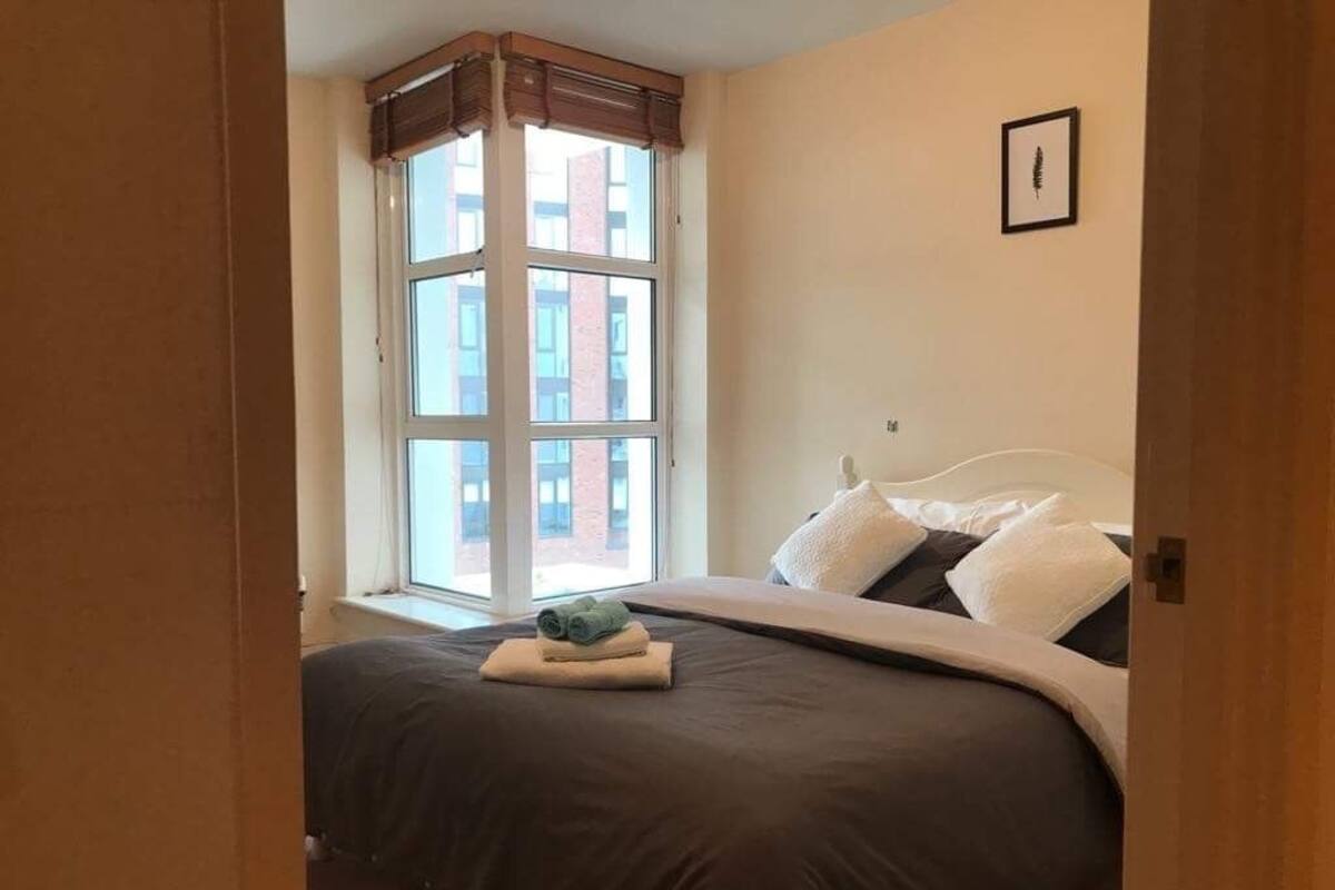 A bedroom with a large bed, a window with blinds, and a framed picture on the wall.