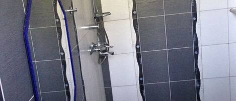 Un baño con lavamanos blanco, espejo y ducha con cabezal de ducha manual.