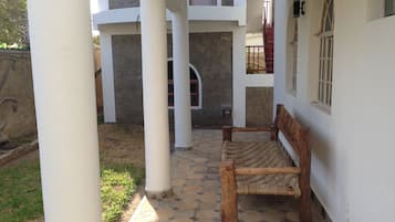 Un patio cubierto con banca de madera, pilares blancos y suelo de baldosas.