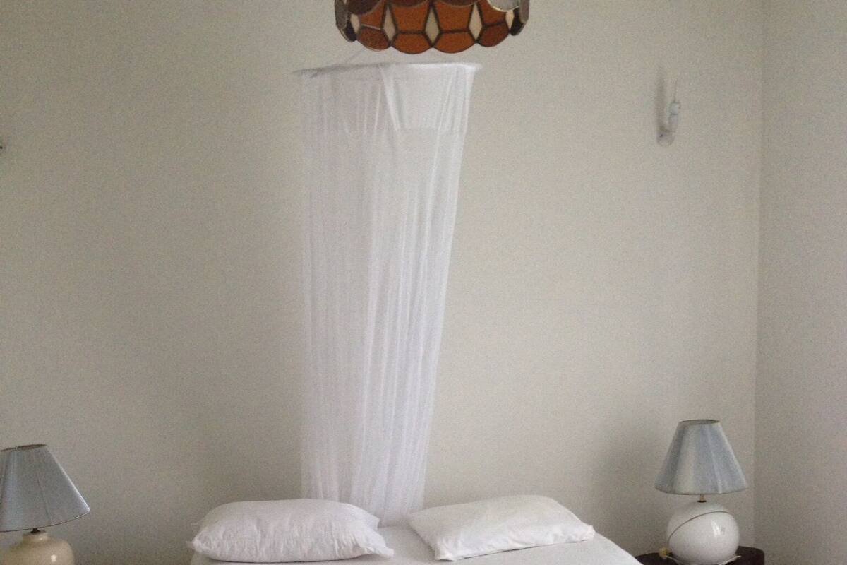 A bedroom with a bed, white bedding, a canopy, two bedside tables with lamps, and a hanging light fixture.