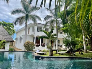 A resort with a swimming pool, palm trees, and a white building with balconies. - Coco-De-Ville (Diani Beach)