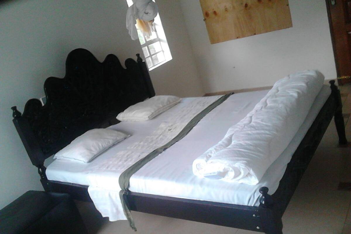 A single bed with white linens, a wooden headboard, and a window with curtains.