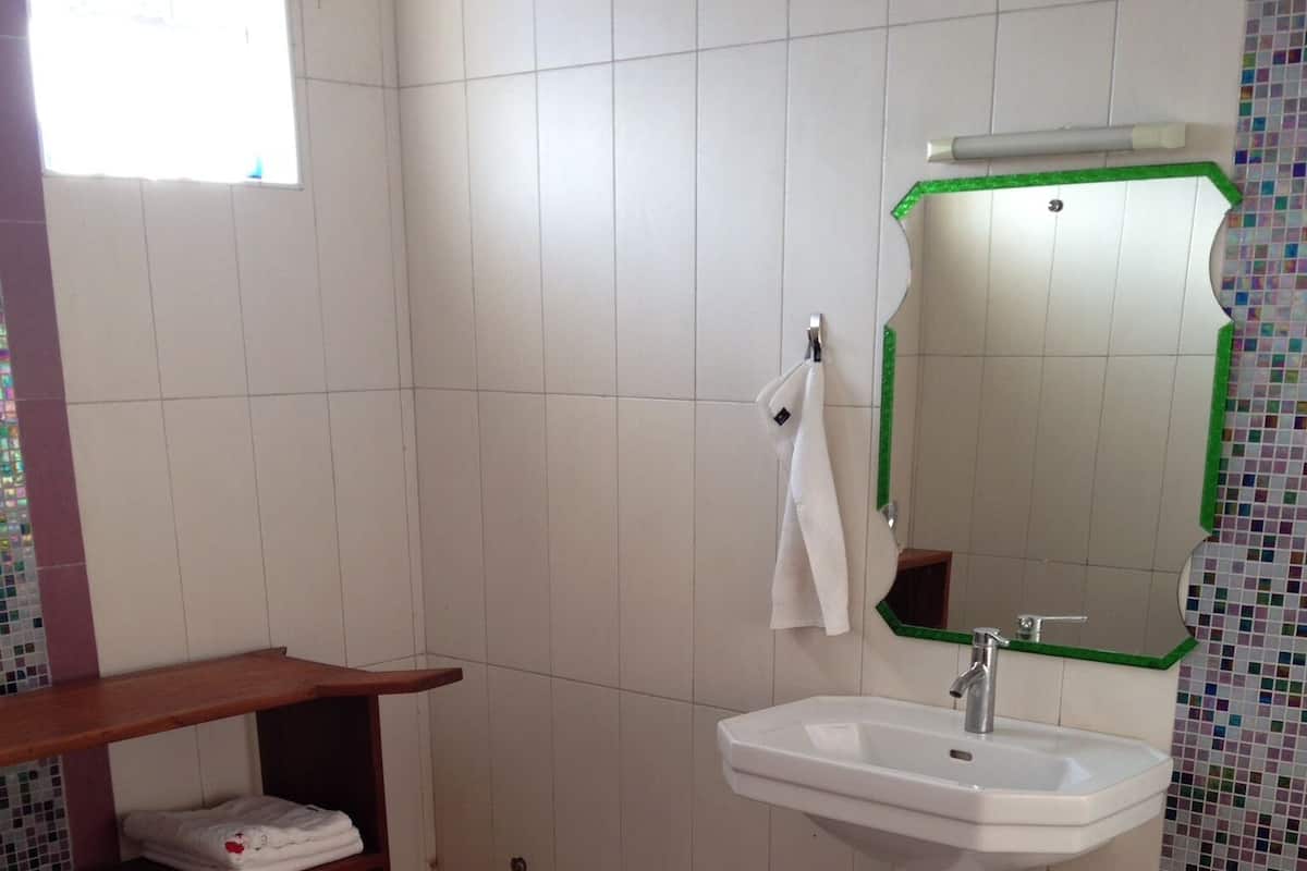 A bathroom with a white sink, a mirror, a toilet, a shelf with towels, and a patterned floor.