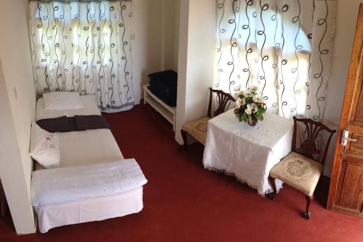 A room with a bed, a small table with a vase of flowers, a chair, and a wooden cabinet.
