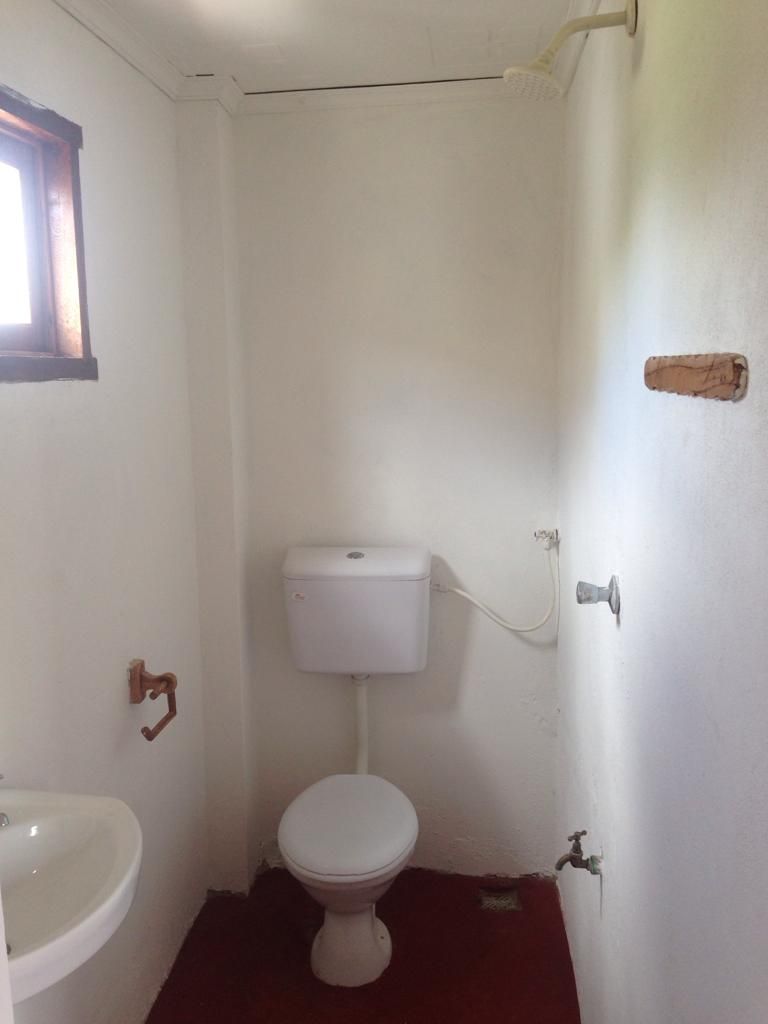 Une petite salle de bain blanche, avec des toilettes, un lavabo et une fenêtre.