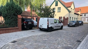A cobblestone street with parked cars and a white van with a sign. - Hotel Am Rathaus (Tangermünde)