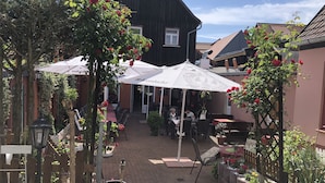 An outdoor café area with tables and chairs under white umbrellas, surrounded by potted plants and flowers. - Hotel Am Rathaus (Tangermünde)