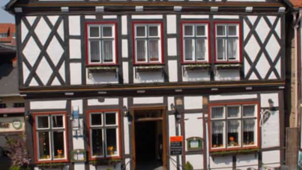 A traditional half-timbered house with a steeply pitched roof, multiple windows with red frames, and a small front entrance. - Hotel Am Rathaus (Tangermünde)