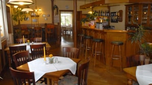 A restaurant interior with wooden tables and chairs, a bar area with stools, and hanging pendant lights. - Hotel Am Rathaus (Tangermünde)