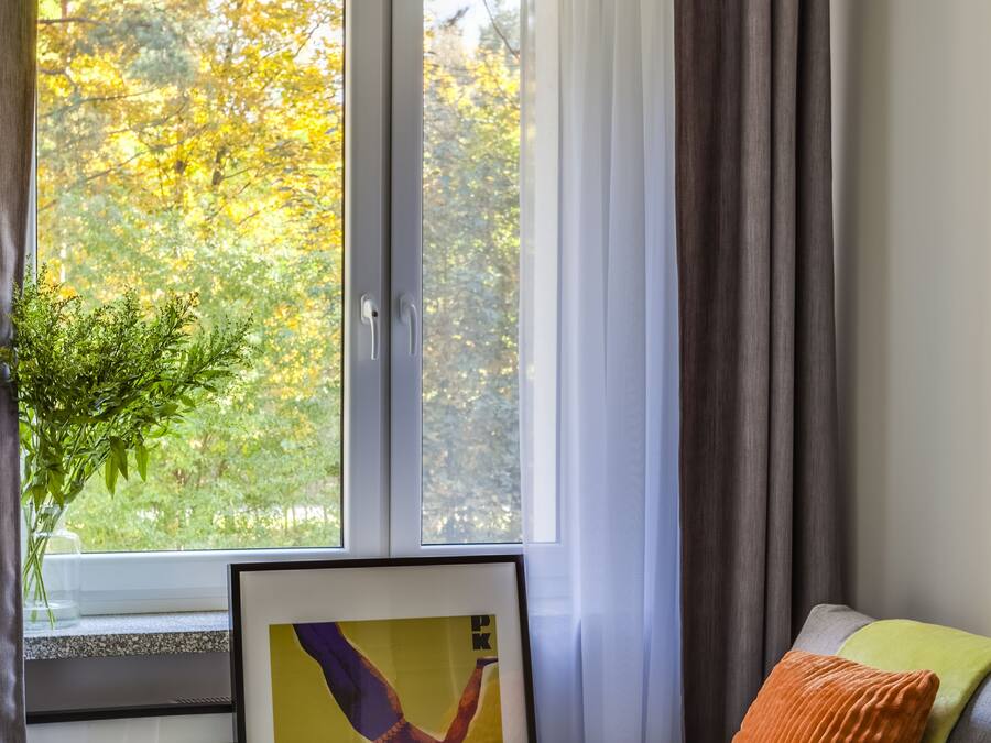 Una habitación acogedora con sofá, una mesita con bandeja, un cuadro enmarco y una ventana con cortinas.