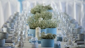 Una mesa dispuesta con cristalería transparente, candelabros azules y pequeñas macetas.