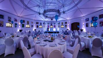 A banquet hall with round tables, white chairs, and blue balloons.