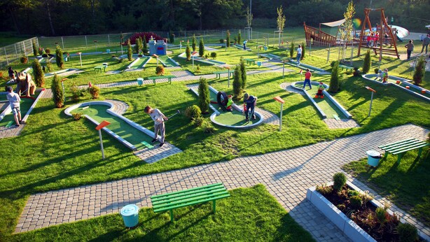 Un campo de mini golf con un diseño sinuoso, bancos verdes y una zona de juegos.